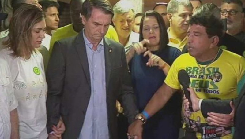 Fuentes: Rebelión [Imagen: Momento de oración convocado por Magno Malta -el senador que lleva la camiseta amarilla en la que se puede leer "Brasil por encima de todo, Dios por encima de todos" -un lema de tradición fascista-, en el que participaron Jair Bolsonaro y su mujer Michelle y otros miembros de su equipo, como Hélio Negao, Luiz Carlos Heinze, Gustavo Bebianno y Alexandre Frota, el 28 de octubre de 2018, el día en que resulto ganador en las elecciones presidenciales brasileñas. Créditos: fotograma de la noticia difundida en TV Globo]