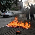 Un manifestante alza el puño frente a una bandera y una gorra estadunidenses en llamas durante una protesta en espera de los resultados de las elecciones presidenciales hondureñas frente a la embajada estadunidense en Tegucigalpa el 23 de diciembre de 2025. Foto Afp