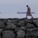 Hombre camina en la orilla de Khor Fakkan (EAU) con petroleros alineados en el estrecho de Ormuz. Altaf Qadri / AP