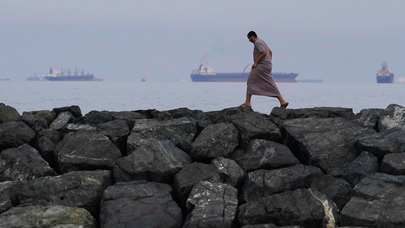 Hombre camina en la orilla de Khor Fakkan (EAU) con petroleros alineados en el estrecho de Ormuz. Altaf Qadri / AP