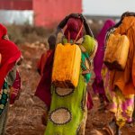 El agua y la ilusión de la igualdad de oportunidades Tres mujeres con ropas de colores transportan bidones con agua en la espalda. Foto: Sntes/Shutterstock.