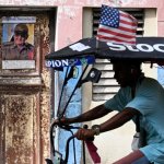 Un hombre en bicicleta pasa frente a una puerta desgastada donde se exhibe una foto del expresidente cubano Raúl Castro en La Habana, el 5 de junio de 2026. Foto Afp