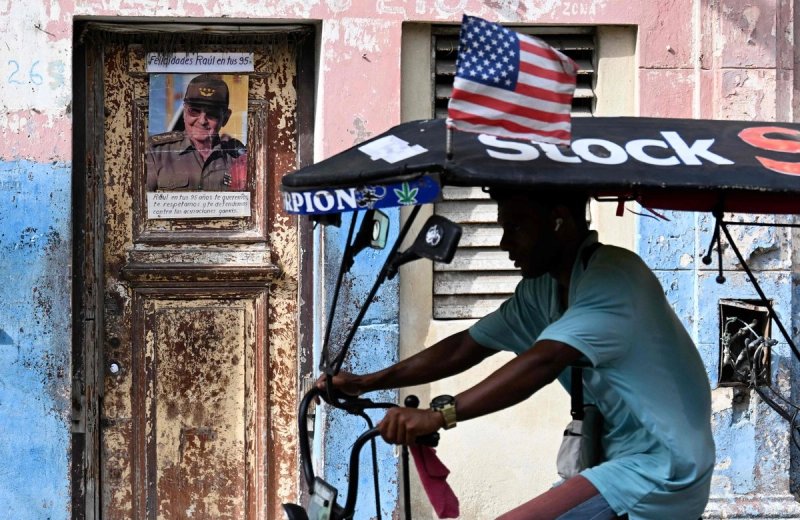 Un hombre en bicicleta pasa frente a una puerta desgastada donde se exhibe una foto del expresidente cubano Raúl Castro en La Habana, el 5 de junio de 2026. Foto Afp